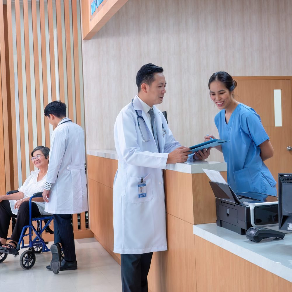 At hospital hall patient sit waiting information counter doctor speaking to administrative crew