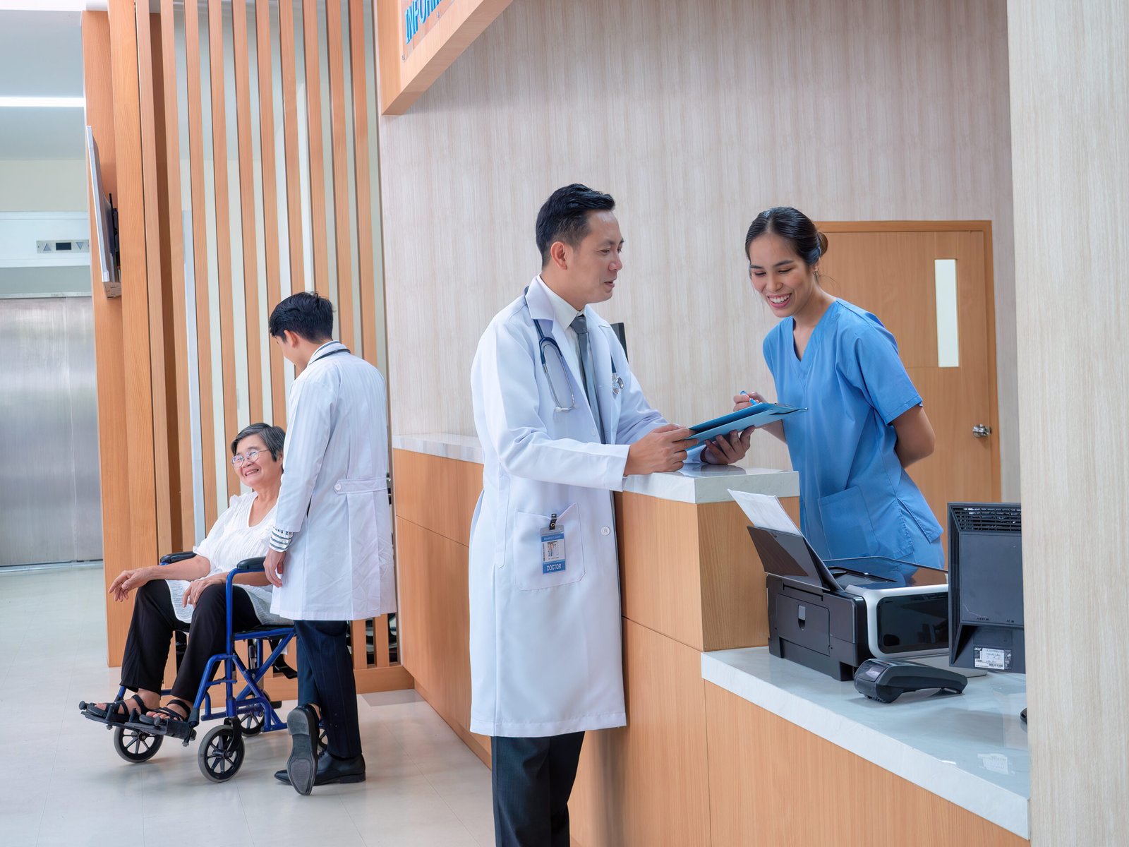 At hospital hall patient sit waiting information counter doctor speaking to administrative crew At hospital hall patient sit waiting information counter doctor speaking to administrative crew