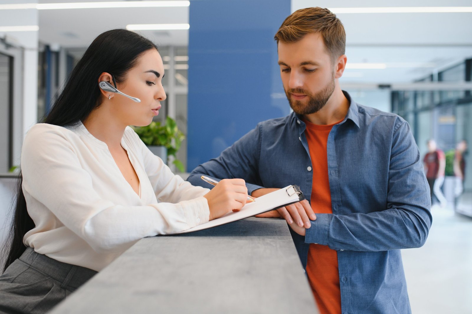 The employee of the beauty salon meets the client in the reception of a modern beauty salon. A man signs a paper with the consent for maintenance. The woman smiles at him The employee of the beauty salon meets the client in the reception of a modern beauty salon. A man signs a paper with the consent for maintenance. The woman smiles at him.